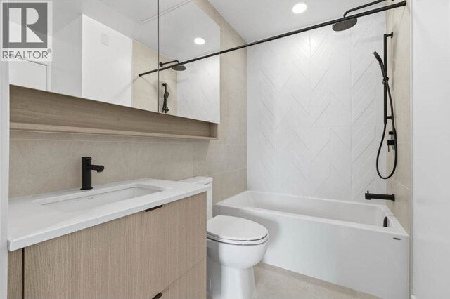 The bathroom, a deep tub under a white patterned tile surround with black fixtures and a rain shower head, a light wood-tone 