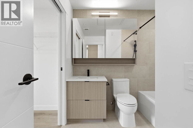 The bathroom from the hall, a sliding pocket door open to the walk-in closet, the vanity and mirrored cabinet with the tub to