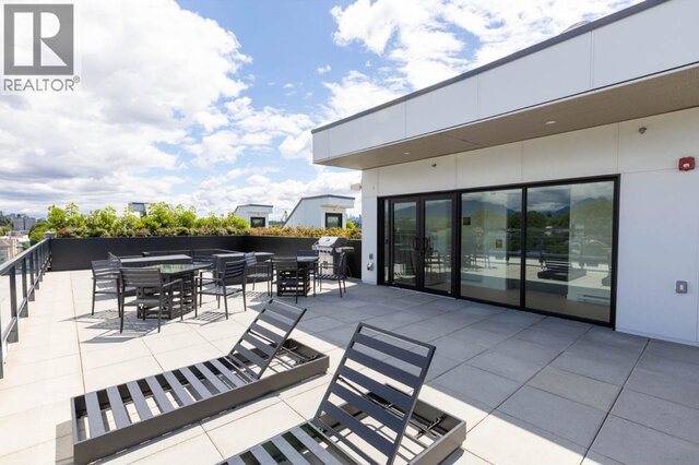 The shared rooftop patio, dining tables and chairs, a barbecue and two loungers in front of the lounge doors.