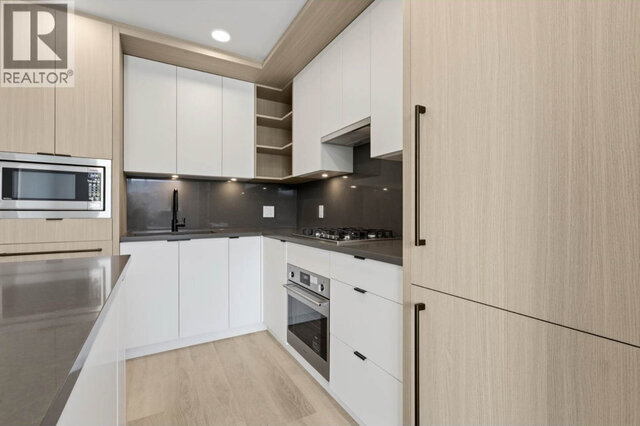 The kitchen close up, a four-burner gas cooktop and wall oven, the built-in microwave, open shelves and under-cabinet lightin