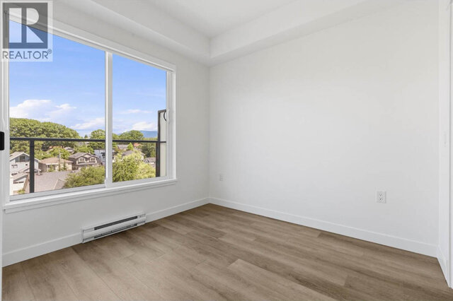 The empty bedroom, a large sliding window onto the balcony with rooftops, trees and hills beyond, light vinyl plank floors.