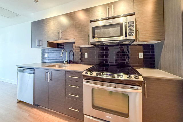 Close view of the range, over-range microwave, dishwasher and glossy black subway tile. - 302-1533 East 8th Avenue, Vancouver East Side