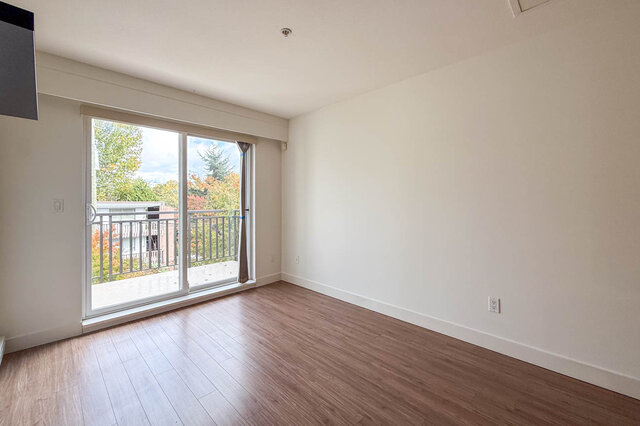 Living room corner with a sliding door onto the balcony and autumn trees outside. - 302-1533 East 8th Avenue, Vancouver East Side