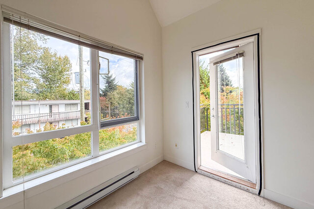 Bedroom corner with a large window and an open door to a balcony surrounded by autumn trees. - 302-1533 East 8th Avenue, Vancouver East Side