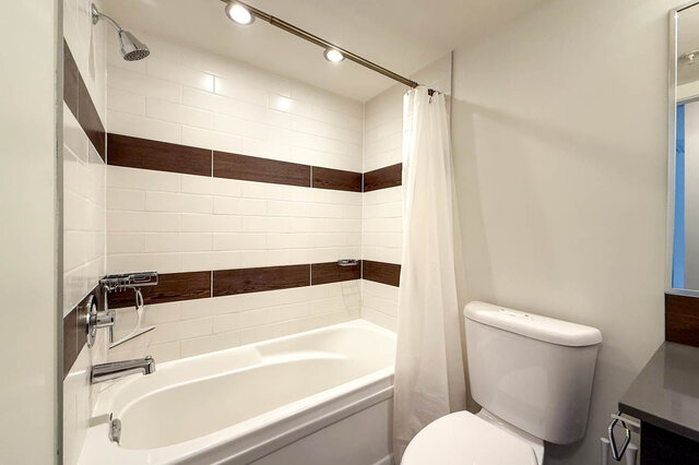 Bathroom with a tub and shower, white subway tile with dark wood-look accent stripes. - 302-1533 East 8th Avenue, Vancouver East Side