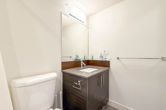 Bathroom vanity with a dark cabinet, grey counter, large mirror and glass shelf. - 302-1533 East 8th Avenue, Vancouver East Side