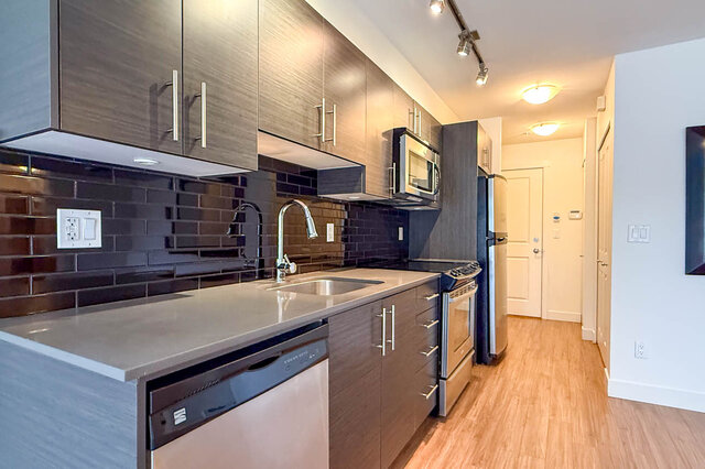 Kitchen counter with an undermount sink and pull-down faucet, glossy black subway tile and dark cabinets.