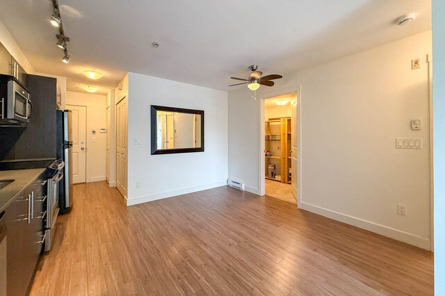 Living area looking back to the front door and closets, with a ceiling fan, a large mirror and the den door open.