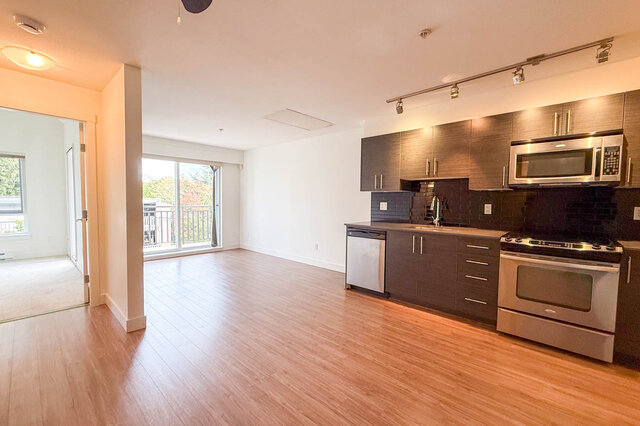 Open living area with the kitchen, dishwasher and range along the wall, track lighting, the bedroom doorway and the balcony d