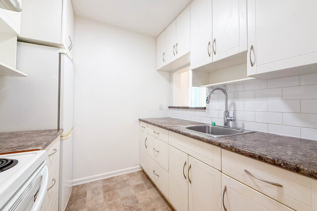The kitchen sink under a small window with white shaker cabinets and a white subway tile backsplash - 107-461-16th Street West, North Vancouver
