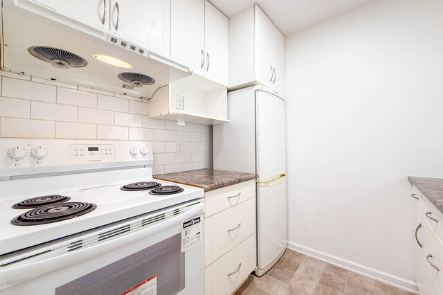 The white stove and fridge under white cabinets, with a subway tile backsplash - 107-461-16th Street West, North Vancouver