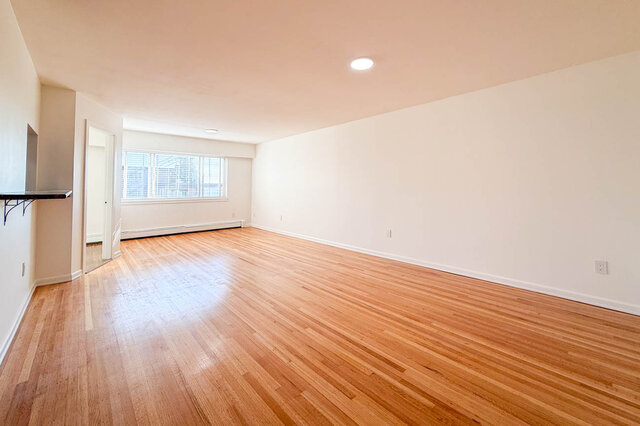 The long living and dining room with hardwood floors, a large window at the end and a pass-through counter to the kitchen