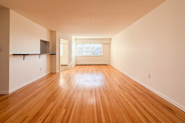 The long living and dining room with shining hardwood floors, a pass-through counter and a large window at the far end