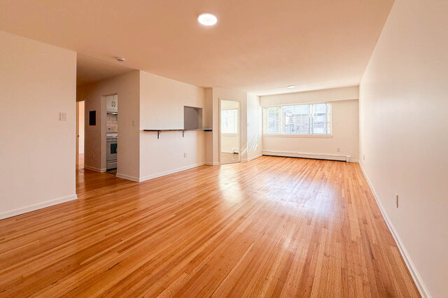 The open living and dining room with hardwood floors and a large window, the kitchen and hallway on one side