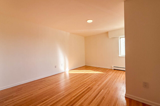 The larger bedroom with sun on the hardwood floors and a window in the corner - 107-461-16th Street West, North Vancouver