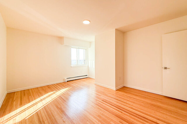 The larger bedroom with a window and sunlight across the hardwood floors - 107-461-16th Street West, North Vancouver