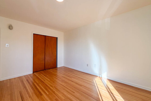 The larger bedroom's sliding wood closet, with sunlight on the floor - 107-461-16th Street West, North Vancouver