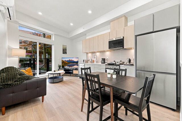 Living and dining space with a table for four, the leather sofa and a patio door with transom glass, the kitchen and stainles