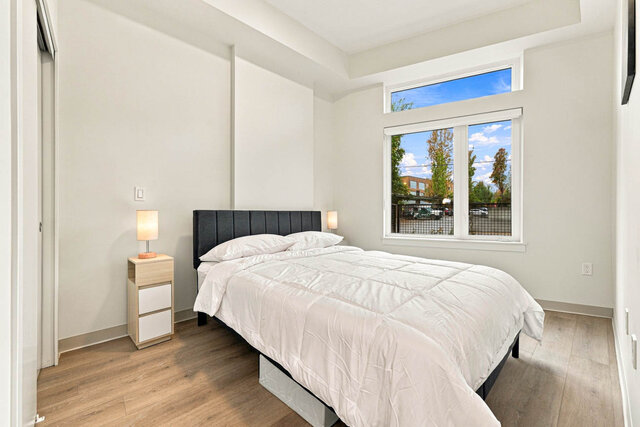 Primary bedroom with a made-up queen bed, two nightstands and a big window with transom glass onto the street trees.