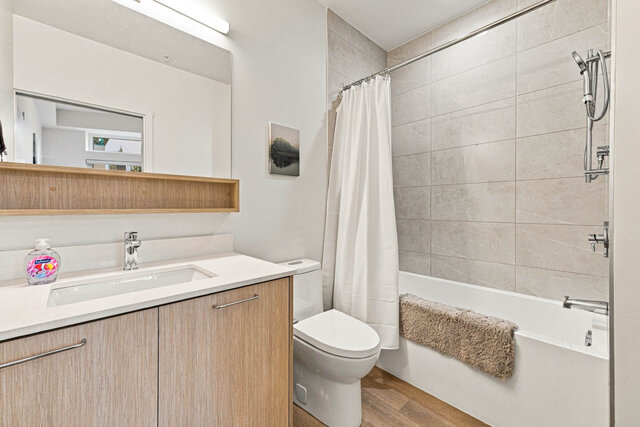 Full bathroom with a tub and shower, tile surround, a light wood vanity and an open shelf under the mirror. - 111-1529 Oxford Street, North Vancouver