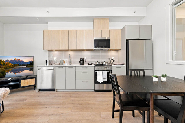 Kitchen wall with light oak cabinets, under-cabinet lighting, a dishwasher, range, microwave and stainless fridge, the dining