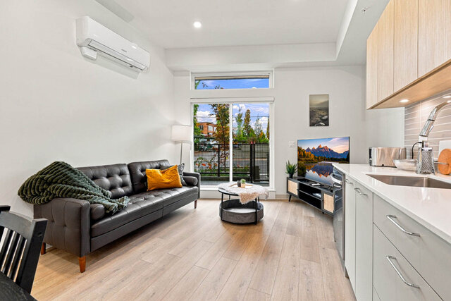 Living room with a leather sofa, wall air conditioning and the patio door with transom glass. - 111-1529 Oxford Street, North Vancouver