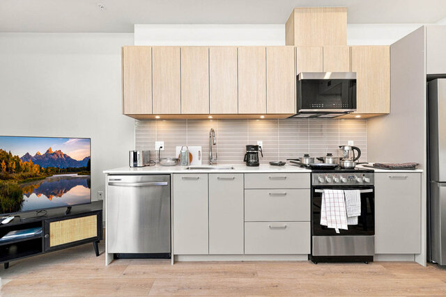 Straight-on kitchen with light oak cabinets, under-cabinet lighting, a dishwasher, range and microwave. - 111-1529 Oxford Street, North Vancouver