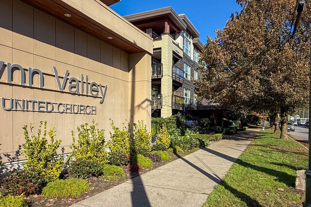 The building beside the Lynn Valley United Church sign, with balconies above a planted sidewalk. - 402-3205 Mountain Highway, North Vancouver