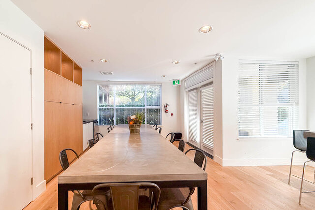 Lounge long table with metal chairs, tall wood cabinets and french doors out to the courtyard. - 402-3205 Mountain Highway, North Vancouver