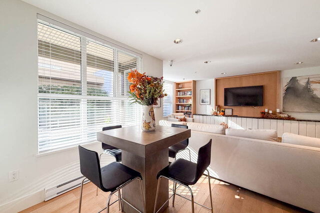 High table with bar stools by the lounge window, the sofa and TV wall behind. - 402-3205 Mountain Highway, North Vancouver