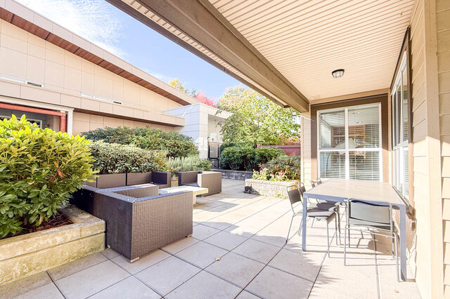 Shared courtyard with wicker lounge seating, a covered outdoor dining table and planted beds. - 402-3205 Mountain Highway, North Vancouver