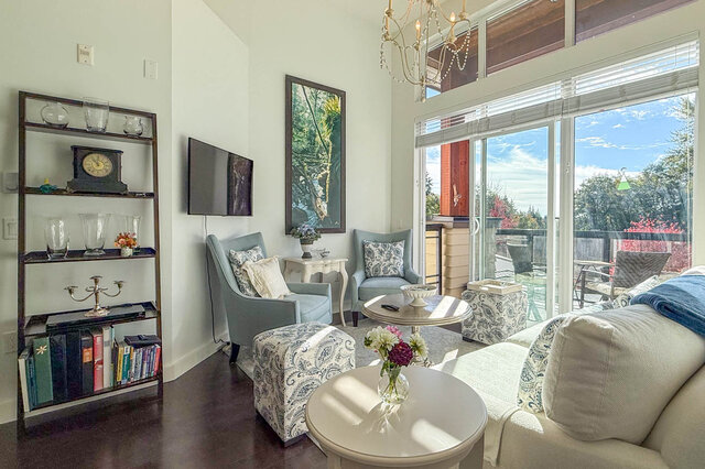 Living room corner with a wall-mounted TV, two armchairs and sliding doors out to the balcony and the trees.
