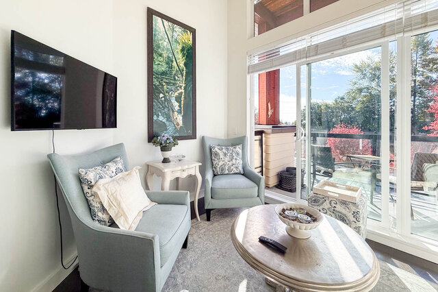 Two armchairs under a wall-mounted TV, beside the sliding glass doors to the balcony. - 402-3205 Mountain Highway, North Vancouver