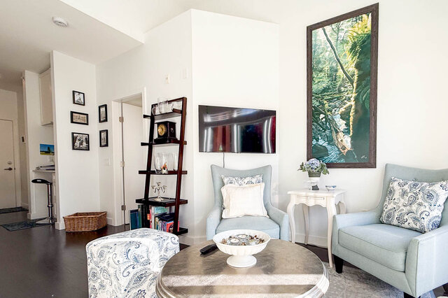 Living room seating with a wall-mounted TV, the hallway to the front door on the left. - 402-3205 Mountain Highway, North Vancouver