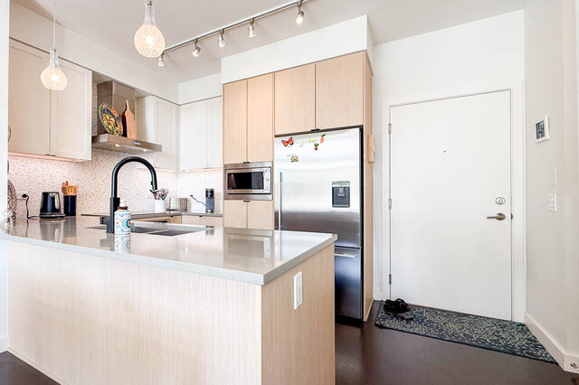 Kitchen peninsula with a double sink, a stainless fridge and built-in microwave, next to the front door. - 402-3205 Mountain Highway, North Vancouver