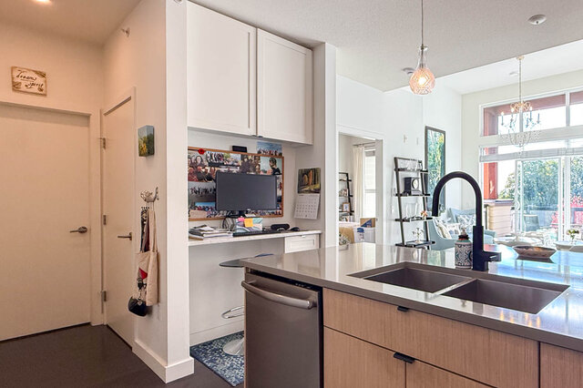 Built-in desk nook beside the kitchen, the double sink in front and the living room beyond. - 402-3205 Mountain Highway, North Vancouver