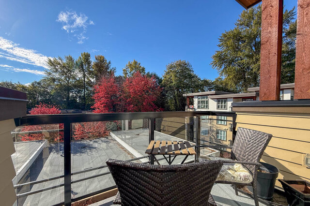 Balcony with wicker chairs and a bistro table looking out over trees and red autumn colour. - 402-3205 Mountain Highway, North Vancouver