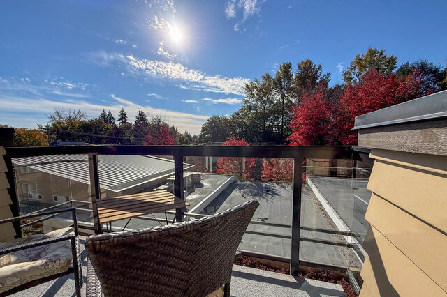 Balcony table and chairs in the sun, trees and red autumn colour past the rooftops. - 402-3205 Mountain Highway, North Vancouver