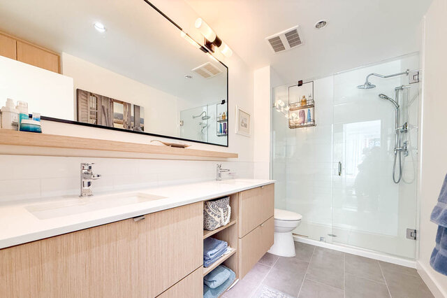 Ensuite bathroom with a double vanity, a big mirror and a walk-in glass shower with a rain shower head. - 402-3205 Mountain Highway, North Vancouver