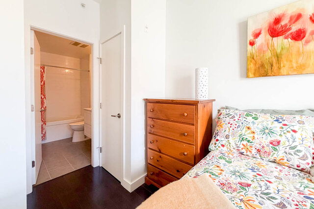 Second bedroom with a dresser, a closet door and its ensuite bathroom with a tub beyond. - 402-3205 Mountain Highway, North Vancouver