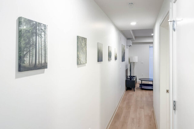 Hallway lined with forest prints leading to the living room, an air conditioning unit at the far end. - 611-1529 Oxford Street, North Vancouver