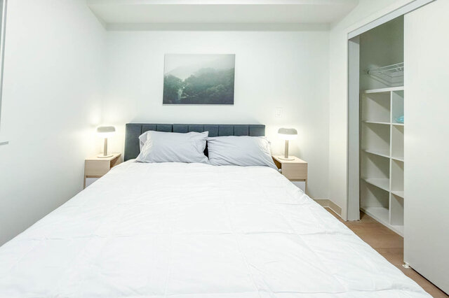 Bedroom with a made-up queen bed, two nightstands with lamps and a closet with built-in shelving. - 611-1529 Oxford Street, North Vancouver