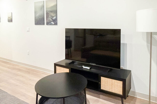 TV on a media console with a round coffee table and a floor lamp. - 611-1529 Oxford Street, North Vancouver
