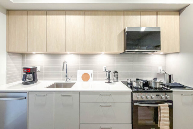 Kitchen with quartz counters, two-tone cabinets, a tile backsplash with under-cabinet lighting, a range, microwave and dishwa