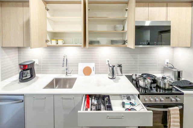 Kitchen with open cupboards of dishes and mugs, a drawer of cutlery, and a kettle, toaster and coffee maker on the counter.