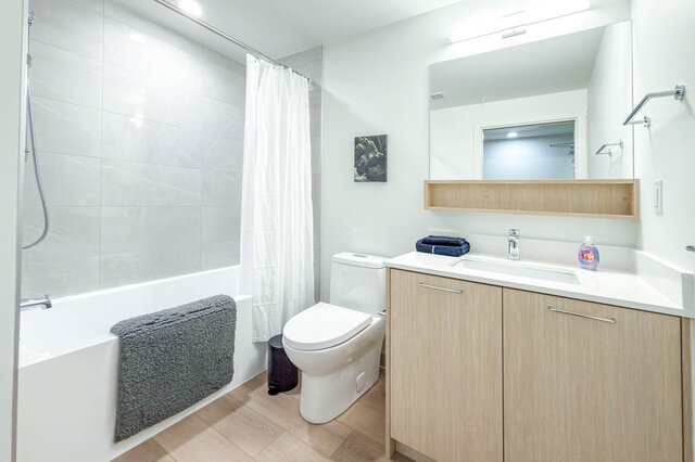 Full bathroom with a tub and shower, tile surround, a light wood vanity and an open shelf under the mirror. - 611-1529 Oxford Street, North Vancouver