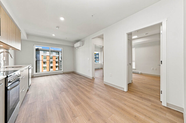 Open living area with a sliding glass door to the balcony, a wall air conditioner and hardwood floors, the kitchen on the lef