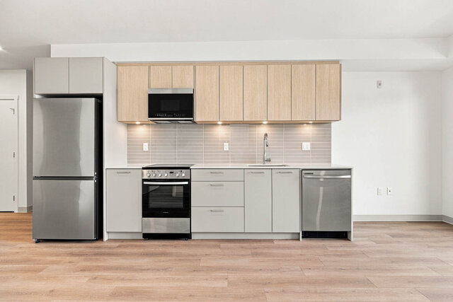 Straight-on kitchen with light oak upper cabinets, grey lower cabinets, under-cabinet lighting, a tile backsplash and a stain