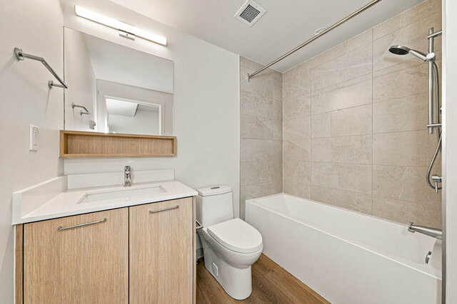 Full bathroom with a tub and shower, a tile surround, a light wood vanity and an open shelf under the mirror.