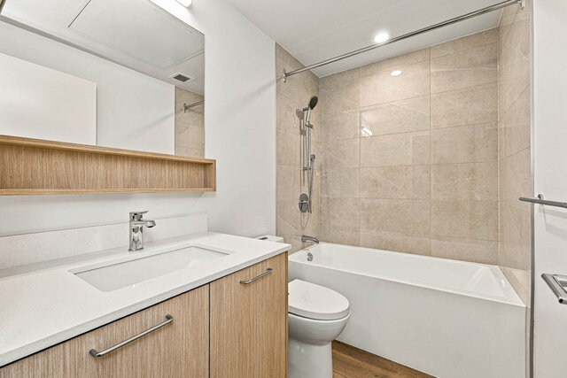 Second full bathroom with a tub and shower, a tile surround and a light wood vanity with a quartz counter. - 525-1529 Oxford Street, North Vancouver
